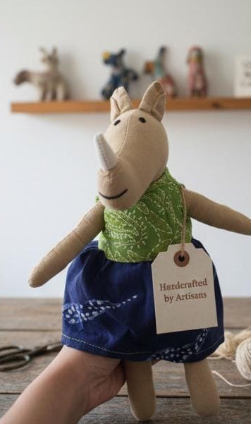 Stuffed animal toy with a green shirt and blue skirt, held by a person in a workshop setting.